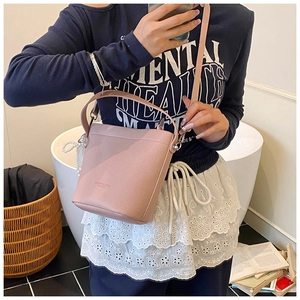 Detail of pink lychee leather bucket bag featuring a decorative pearl charm and shoulder strap