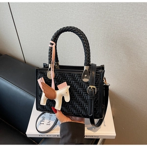 Détail d'un sac à main en cuir tressé noir avec poignées rondes et pendentif pégase