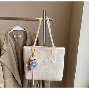 Detail of a beige canvas tote bag with a small bear pendant on a silver metal stand