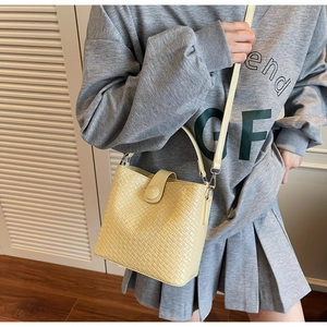 Détail d'un sac seau jaune tissé porté en bandoulière avec texture et sangle à boucle