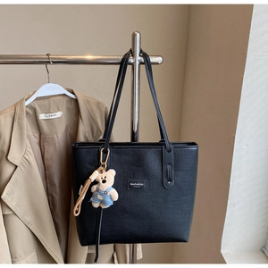 Detail of black woven tote bag featuring a brand leather label and a cute plush bear charm