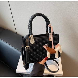 Détail d'un sac cabas en cuir tressé noir avec un charm cheval rose sur livre