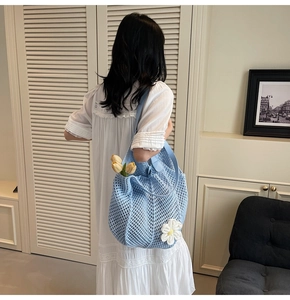 Close-up of light blue crochet tote bag with white flower charm and faux leather handle