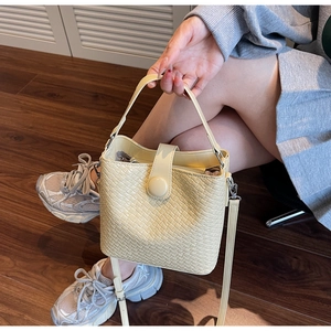 Détail du sac seau tissé beige avec boucle magnétique et texture en cuir synthétique