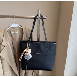 Detail of black woven tote bag featuring a teddy bear charm and metal logo on strap