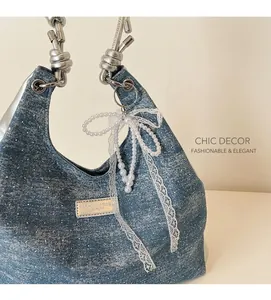 Close-up of blue hobo bag with silver metallic texture, knotted handle and pearl bow charm