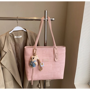 Detail of pink woven tote bag with cute bear charm and branded leather patch decoration