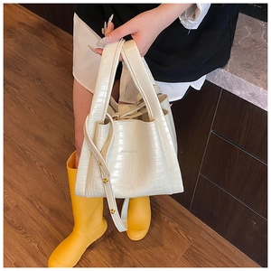 Detail of cream white croc-embossed bucket bag with adjustable strap and top handles