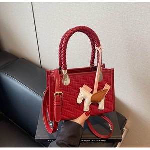 Détail d'un sac à main rouge texturé avec pendentif pégase posé sur des livres de design