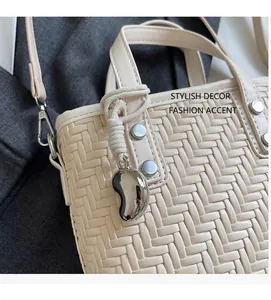 Dettaglio della borsa beige intrecciata con borchie argentate e ciondolo a fagiolo