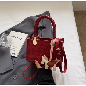 Détail d'un sac bandoulière tressé rouge avec poignée tressée et breloque cheval