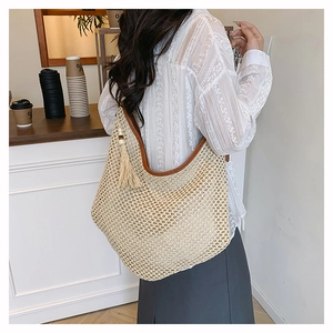 Détail d'un sac à bandoulière en paille tressé avec bordure en cuir et pompon