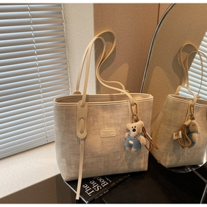 Detail of woven beige tote bag with MashaKeke logo and blue bear plush pendant charm