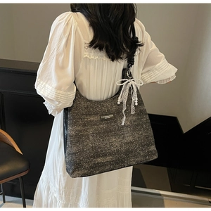 Detail of dark grey tote bag with lace bow, pearl charm, and fashion leather patch