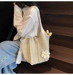 Detail of cream woven tote bag with daisy pendant worn on shoulder in soft lighting