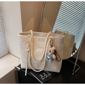 Detail of beige woven tote bag with leather logo tag and cute blue bear keychain