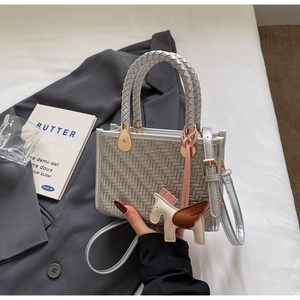 Détail d'un sac à main tissé argenté avec breloque cheval sur un costume gris