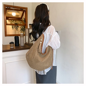 Détail d'un sac de plage en paille tressée avec pompons et bandoulière en cuir