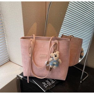 Pink woven tote bag with a leather brand tag and a cute plush bear charm decoration