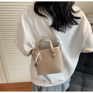 Dettaglio della borsa beige intrecciata con ciondolo a cuore su felpa con cappuccio bianca