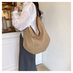 Détail du sac cabas en paille tissée avec anses en cuir marron et décor de glands