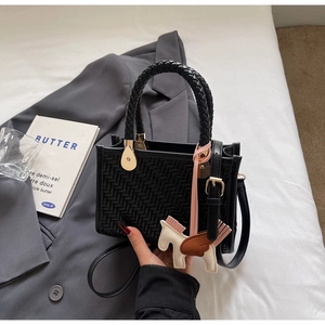 Détail d'un sac à main tressé noir avec breloque cheval sur un blazer gris élégant