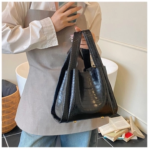 Close-up of black crocodile pattern tote bag with gold-tone bottom rivets and logo detail