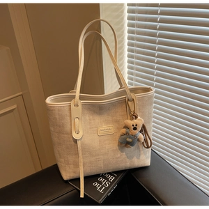 Detail of beige tweed tote bag with leather logo, teddy bear charm and soft sunlight