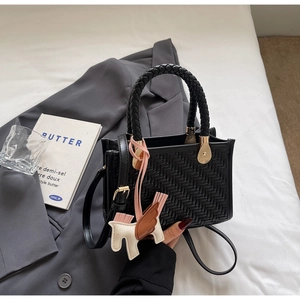 Détail d'un sac à main noir tressé avec poignée torsadée et pendentif cheval décoratif