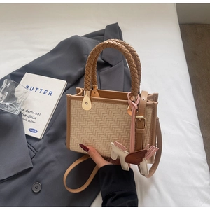 Détail du sac à main en paille tissée avec garniture en cuir, breloque Pégase et bandoulière