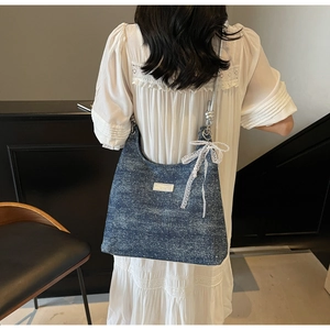 Détails d'un sac baguette en denim bleu avec nœuds en dentelle, perles et bandoulière chaîne