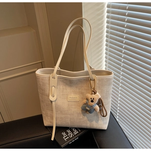 Detail of off-white woven tote bag featuring leather logo patch and cute plush bear charm
