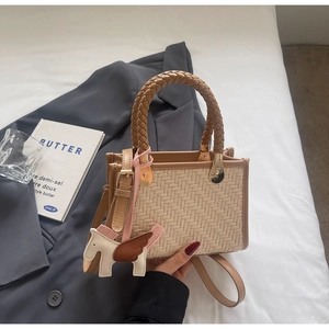 Détail du petit sac carré tissé beige avec poignée marron et accessoire de charme cheval