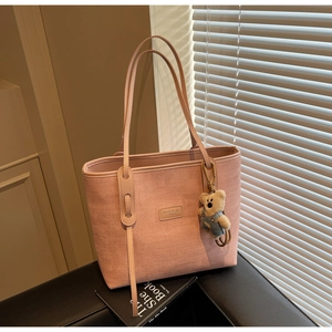 Detailed texture of pink woven tote bag with metallic logo and cute bear pendant