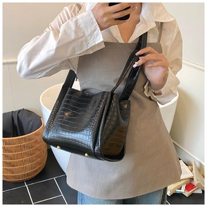 Detail of black crocodile embossed bucket bag with gold metal feet in a lifestyle setting