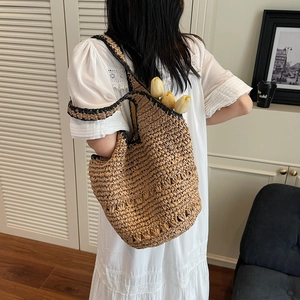 Detail of handwoven straw tote bag with black contrast trim shown in lifestyle setting