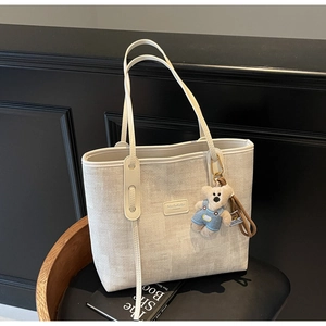 Detail of cream woven tote bag featuring a leather logo patch and cute plush bear charm