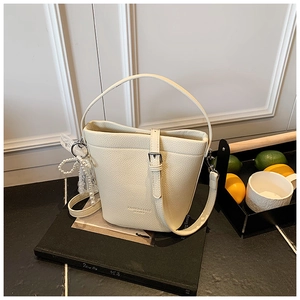 Dettaglio borsa a secchiello beige con trama litchi e ciondolo di perle e pizzo