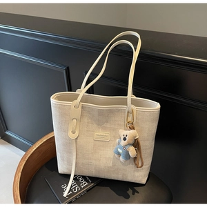 Detail of beige woven tote bag featuring leather handles and cute plush bear charm