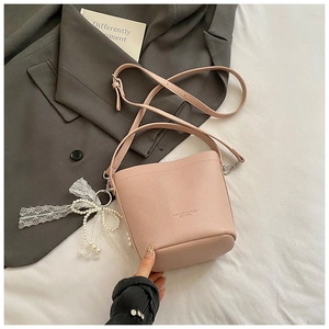 Detail of light pink pebble leather bucket bag with lace bow and pearl charm ornament