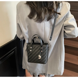 Dettaglio di una borsa a tracolla intrecciata nera con borchie indossata su un blazer