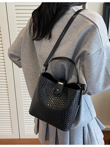 Sac seau tissé noir à la mode avec longue bandoulière porté par un mannequin chic