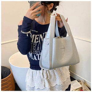 Detail of light blue crocodile embossed tote bag with brand logo and bottom metal studs
