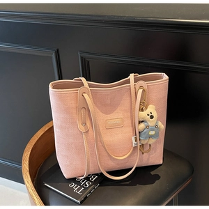 Pink woven tote bag featuring a leather logo patch and a cute teddy bear charm