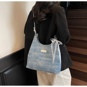 Détail du sac hobo en denim bleu avec ruban en dentelle blanche et charme de perles