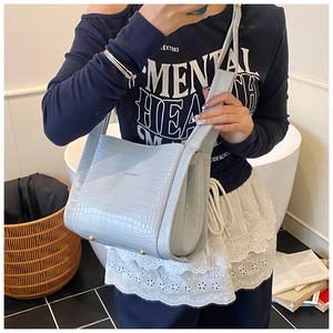 Detail of light blue crocodile pattern bucket bag with protective gold base studs