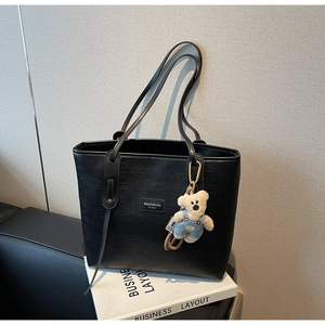 Detail of black woven tote bag with a cute bear plush charm and logo plate on a book