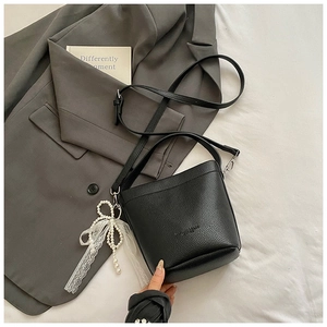 Detail of black pebble leather bucket bag featuring a white pearl bow charm on the side