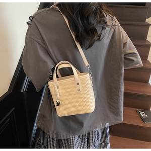 Dettaglio borsa a secchiello intrecciata beige con ciondolo a cuore indossata da modella