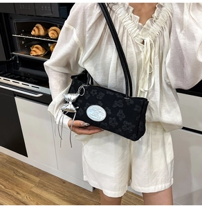 Dettaglio borsa a spalla in nylon nero con rilievo floreale e ciondolo a fiocco argento